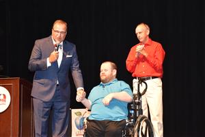 Dr. Nichols welcoming guest speaker Patrick Henry Hughes to stage with Patricks father behind wheelchair